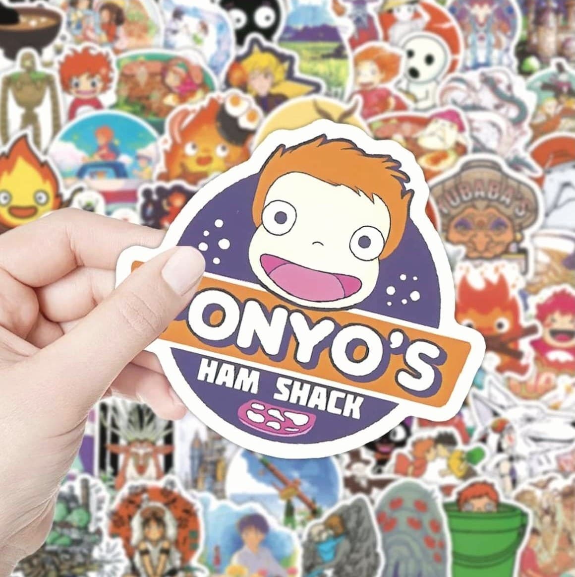 A hand-cut sticker held over a spread of designs